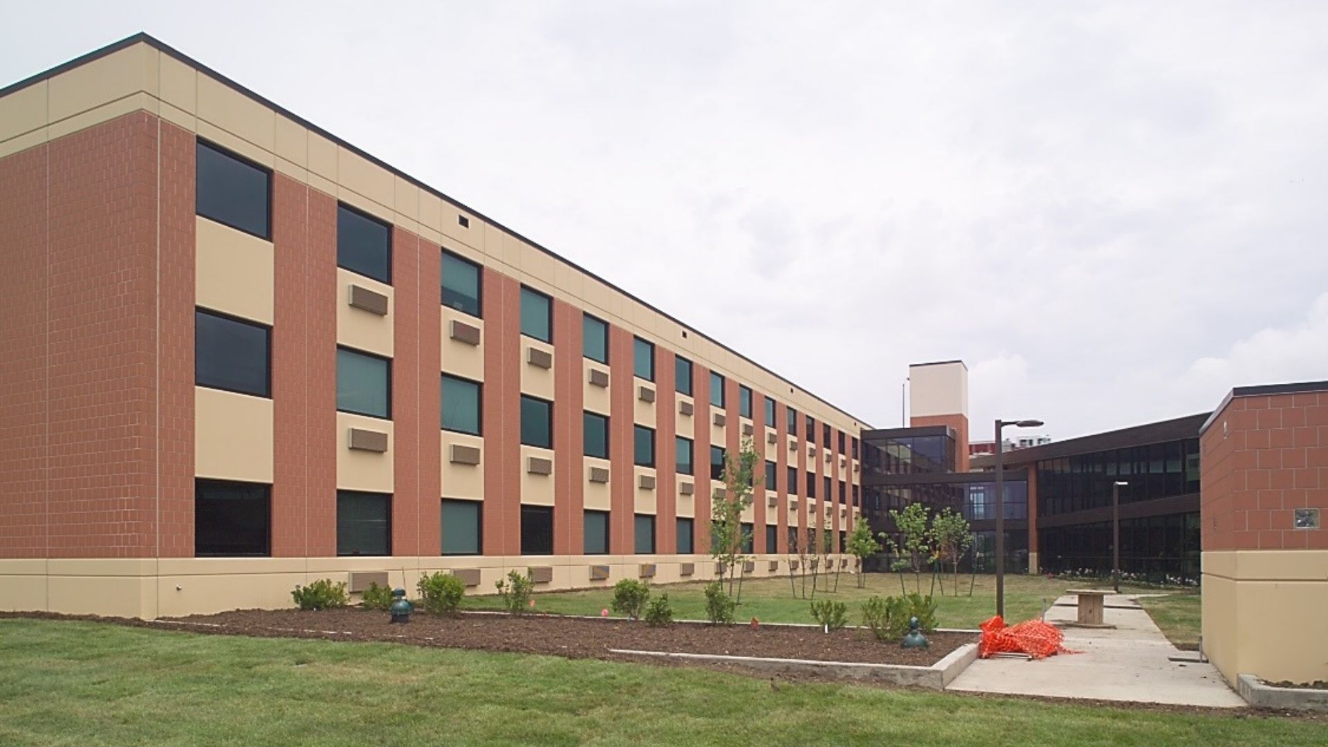 Three-story YMCA supportive housing building with brick and tan siding, rows of windows, and a newly landscaped courtyard.