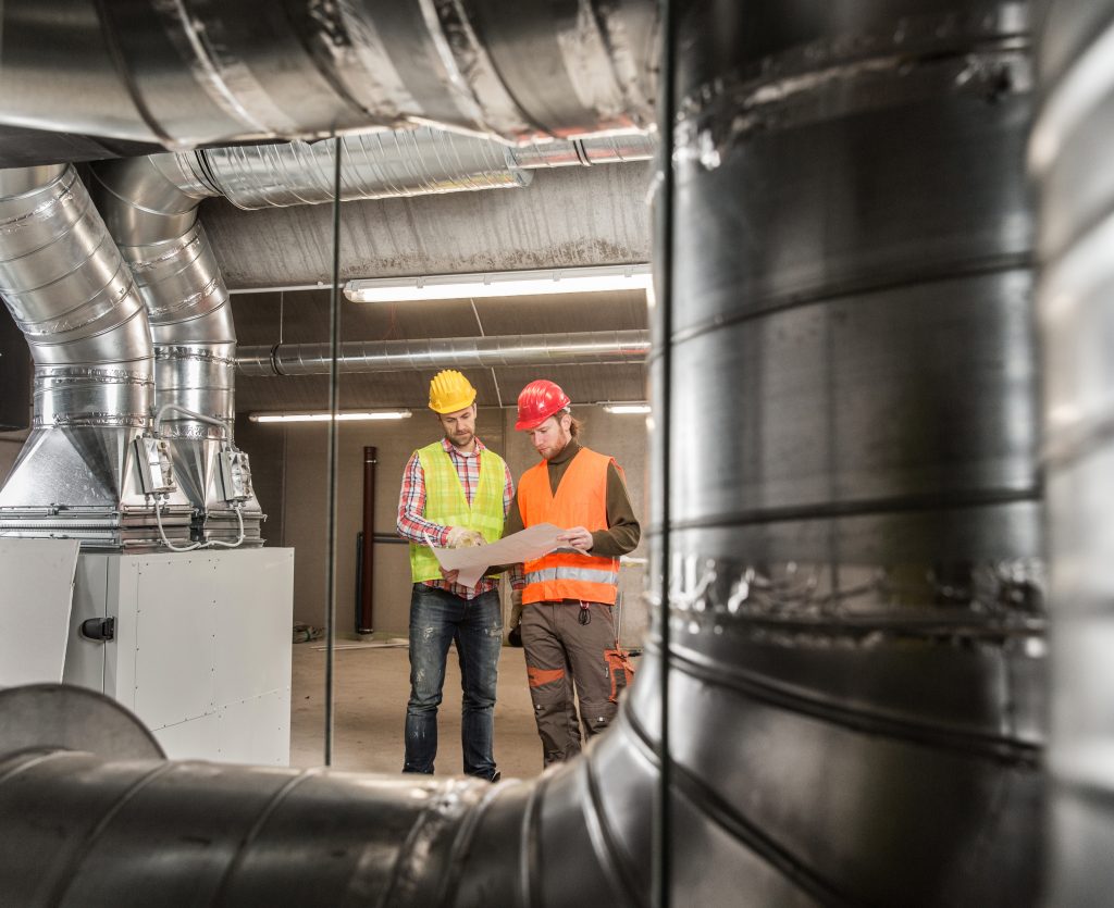 Two workers standing near HVAC pipes
