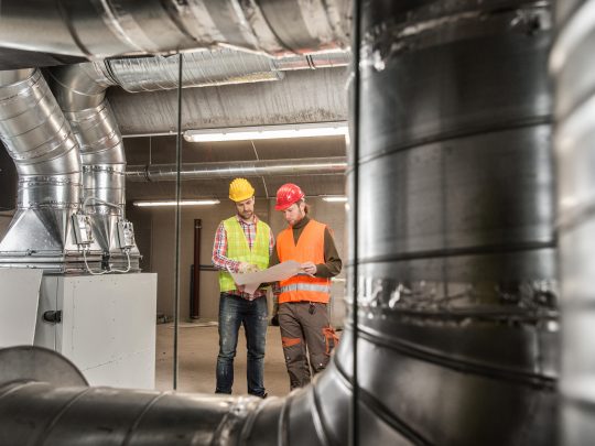 Two workers standing near HVAC pipes