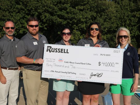 Five Russell employees standing in front of a giant check made out to charity.