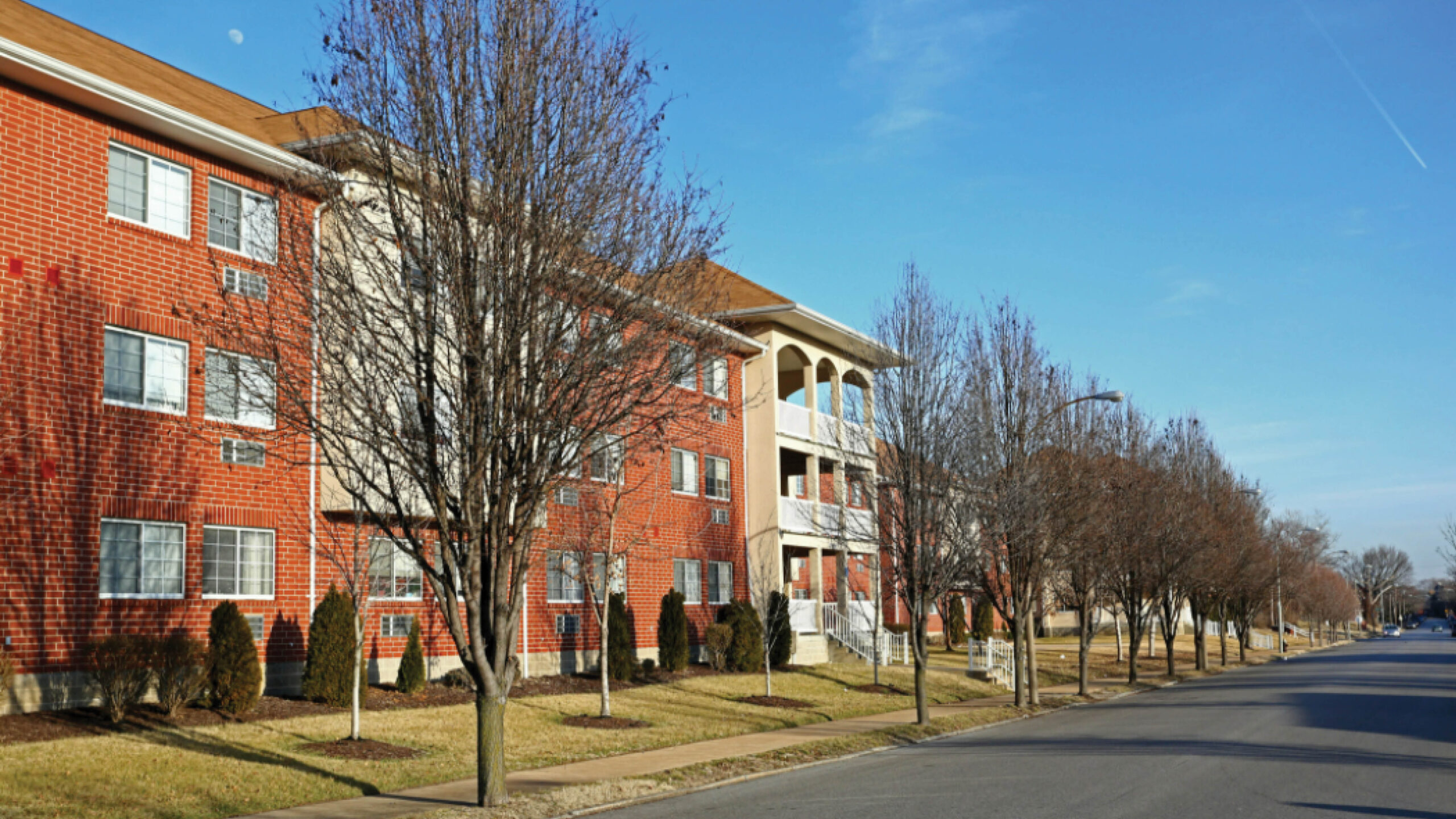 multi-story brick apartment building with balconies and trees
