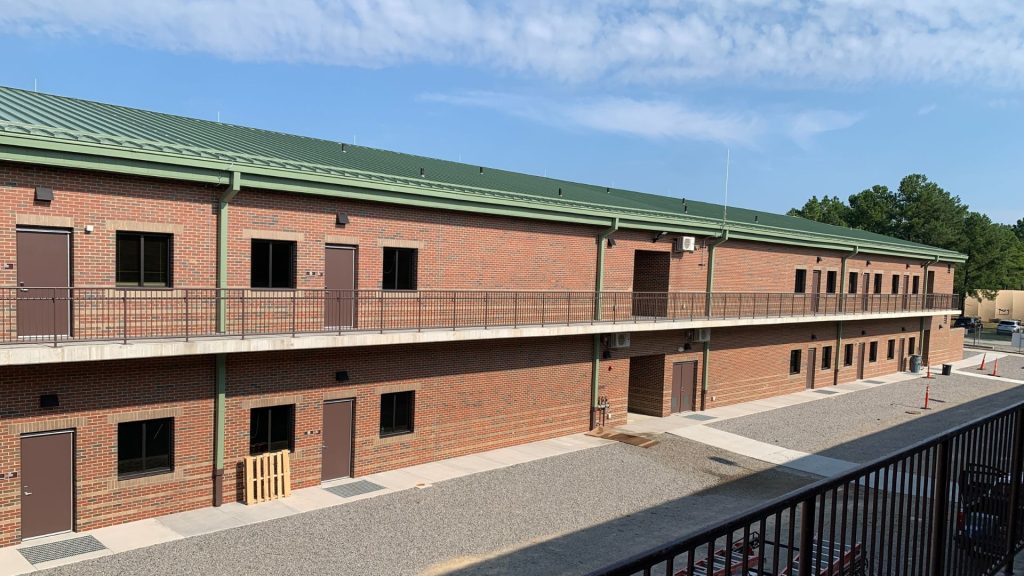 Exterior of the two-story brick Ready Building with green standing seam roof and second-floor walkway at Camp Mackall, NC