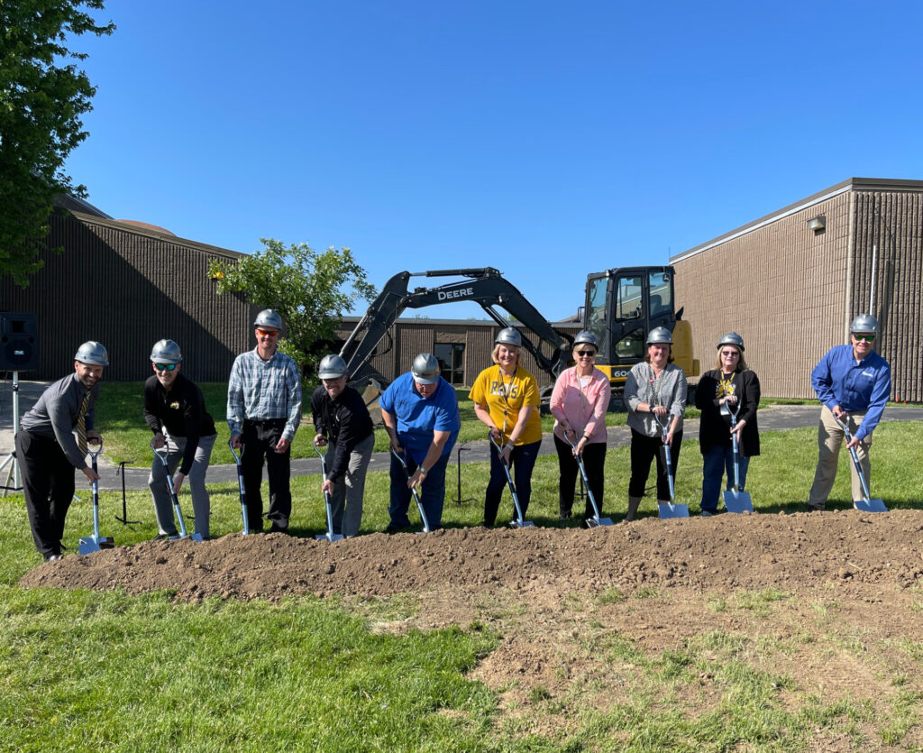 Team holding shovels in dirt smiling