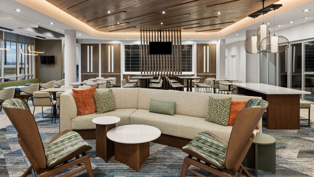 Lobby lounge at the SpringHill Suites by Marriott in Bettendorf, with a curved sofa, wood ceiling, and dining tables.
