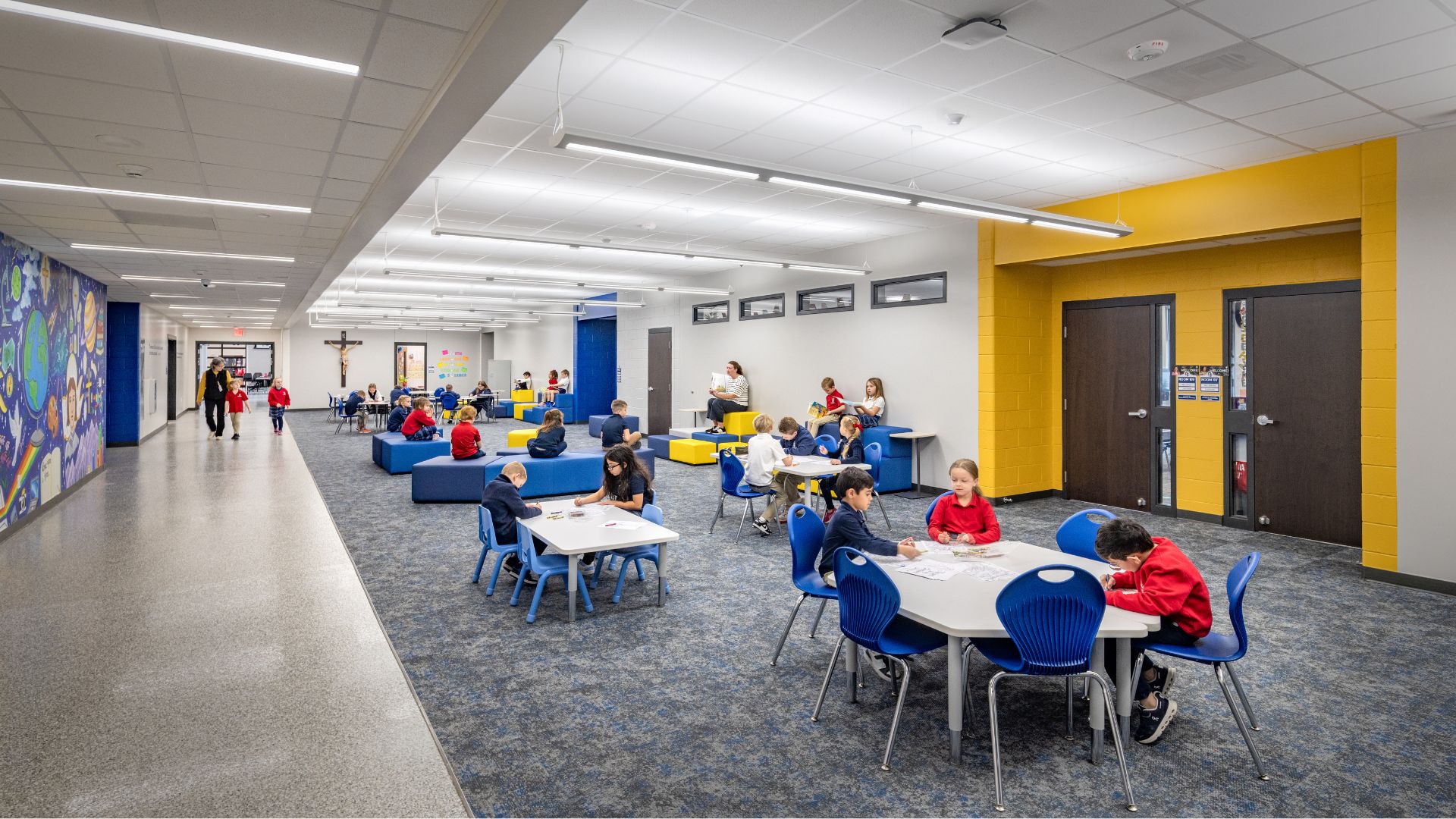 Students reading and working at tables and blue and yellow seating in the student commons at St. Joan of Arc Catholic School.