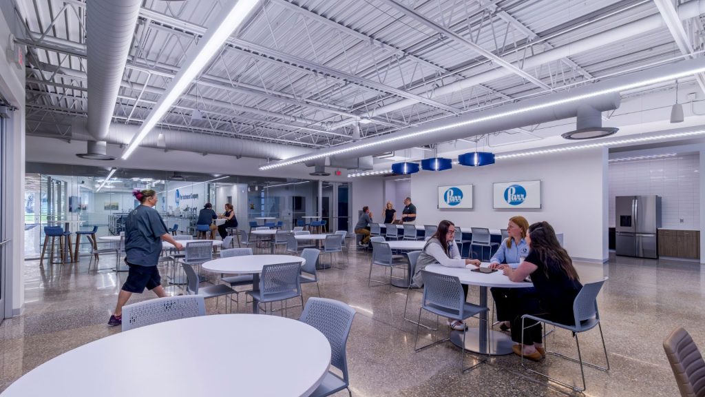 Employee dining area at Parr Instrument Company with round tables, a counter, and a glass-walled lab beyond.