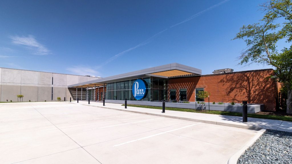 Exterior entrance of Parr Instrument Company in Moline, with a lit Parr sign, glass entry, brick walls, and a canopy.