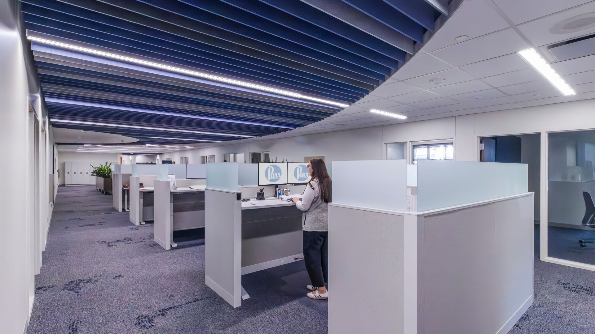 Open office area at Parr Instrument Company with cubicles, a standing desk, and a curved blue baffle ceiling.