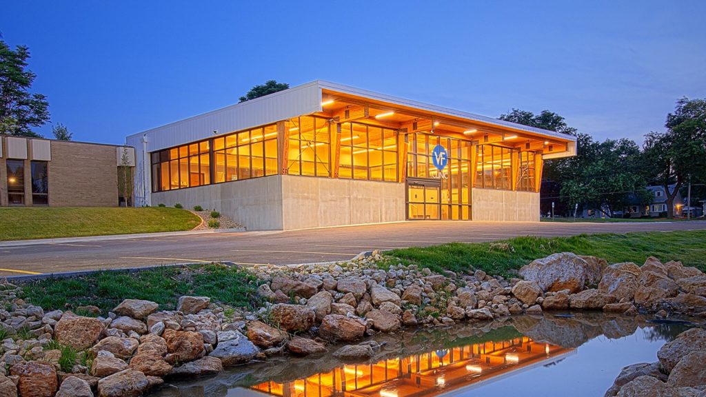 Vera French Clinic glowing at dusk behind a rock-lined pond, with the timber and glass building reflected in the water.