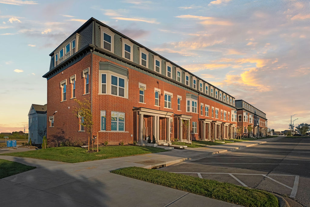 Brick townhome exterior at Village at New Longview with mansard roof, covered entries, and sales office at sunset