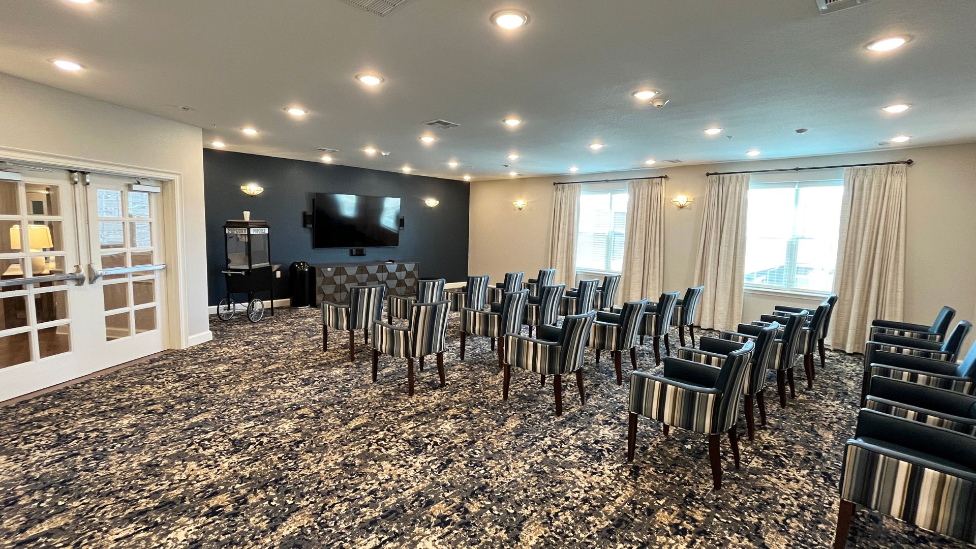 Resident theater room at The Rushwood Senior Living with a wall-mounted TV, striped armchairs, and a popcorn machine
