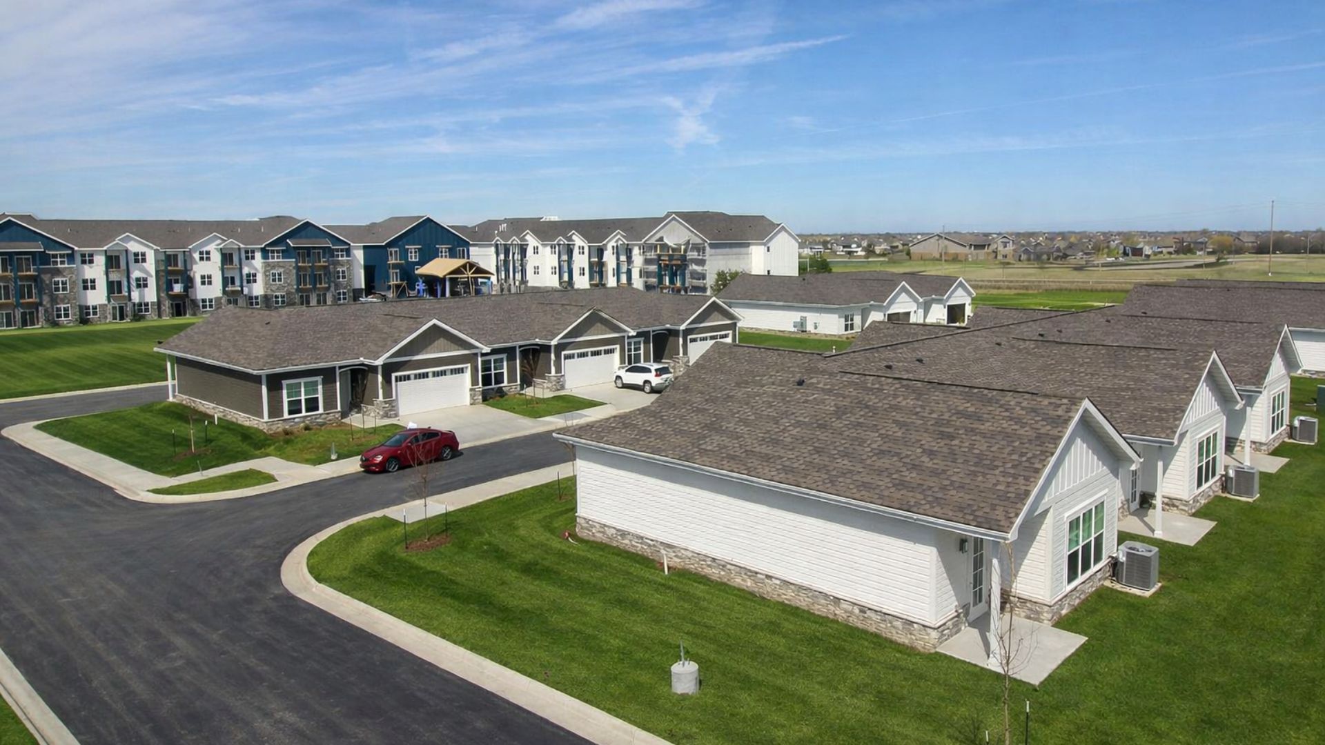 Single-story villas with attached garages at The Rushwood Senior Living, with the multi-story community building in the background