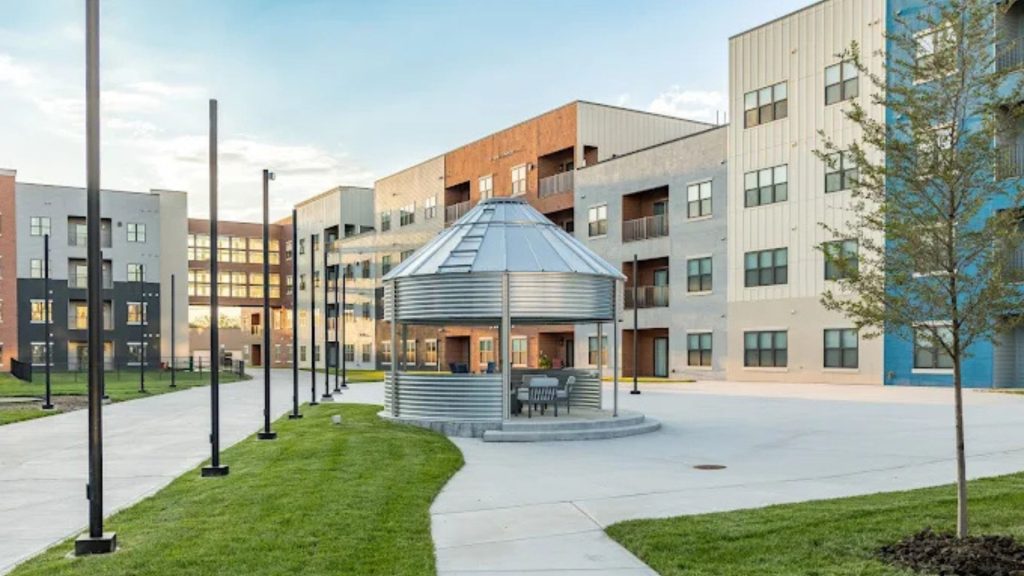 Grain bin-style metal pavilion with outdoor seating in the Union Mill courtyard, surrounded by four-story apartment buildings