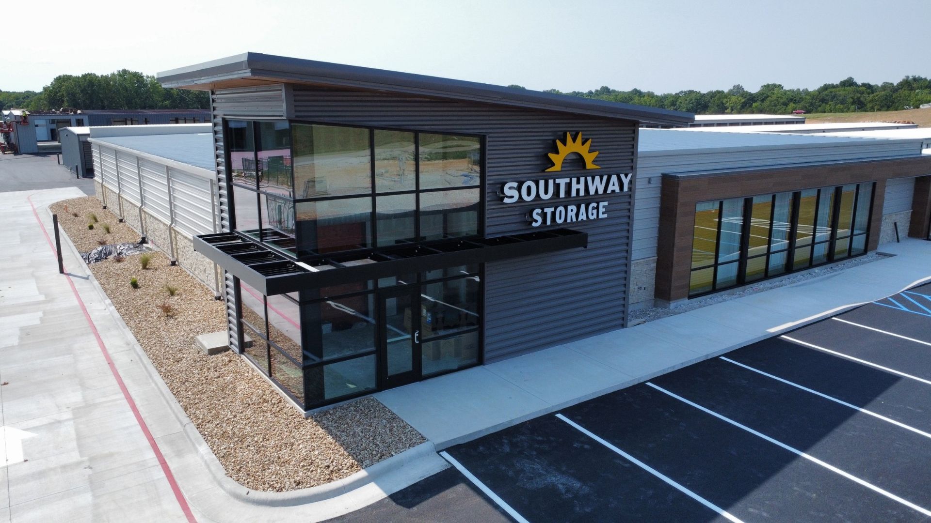 Southway Storage office entrance with corrugated metal siding, a glass storefront, a sunburst logo sign, and a new parking lot.