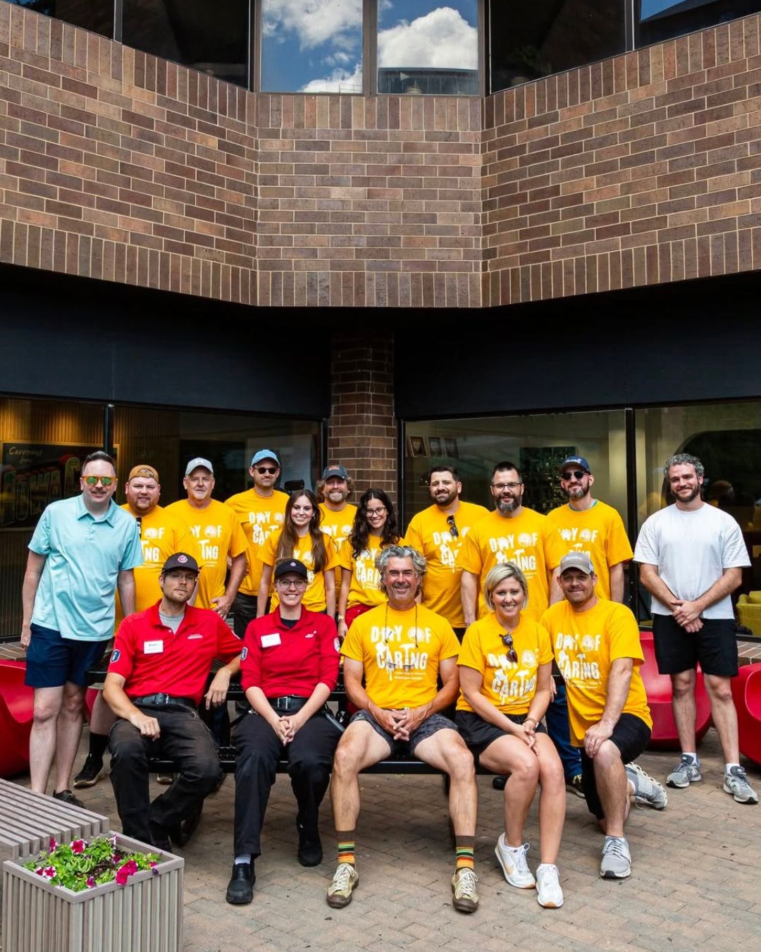 Russell team members in yellow Day of Caring shirts and staff in red uniform shirts pose in a brick courtyard in Iowa City, Iowa